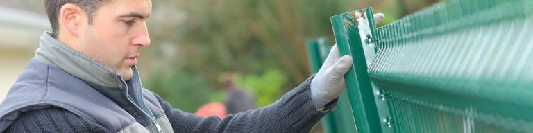 Artisan installant un poteau et un panneau de clôture rigide