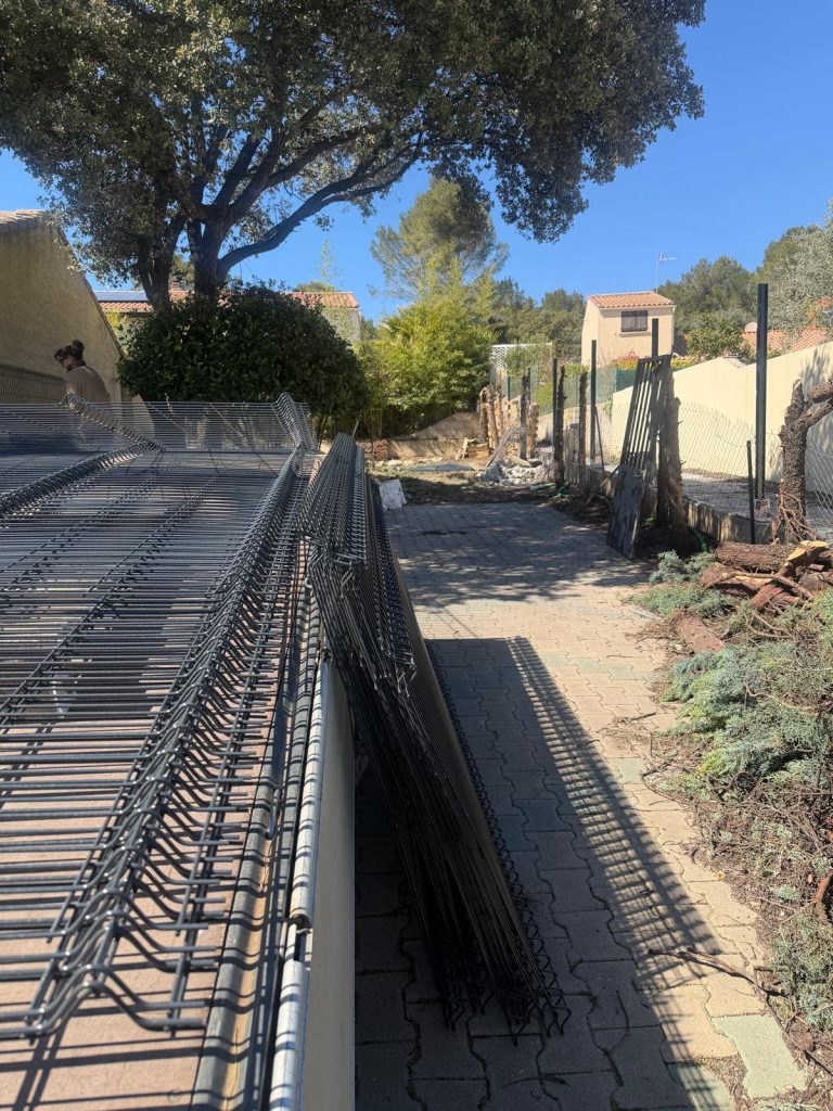 Pose de clôture rigide avec panneaux grillagés sur terrain résidentiel avant scellement des poteaux