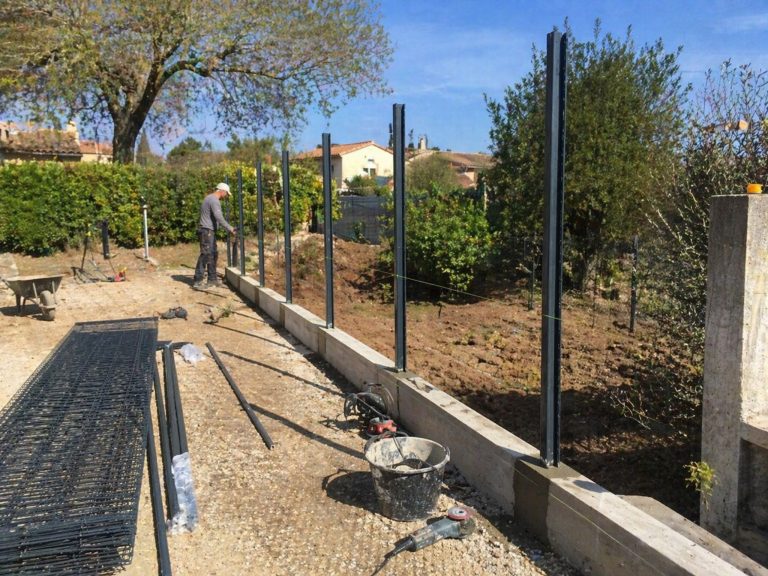 Installation en cours d’une clôture rigide en panneaux grillagés avec poteaux métalliques fixés sur muret béton dans un chantier résidentiel en extérieur